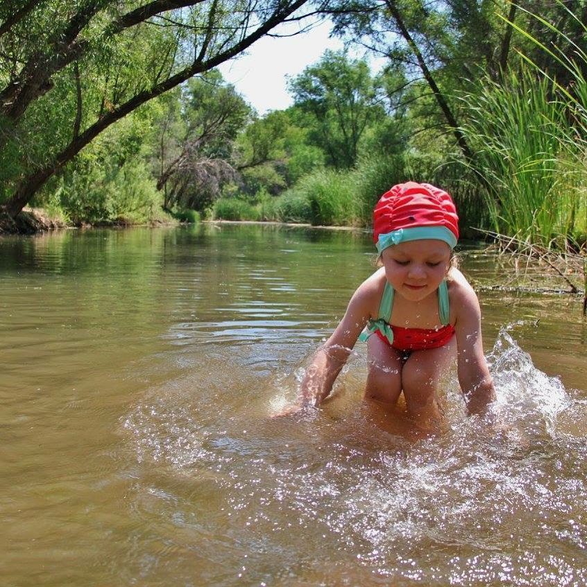 A child plays in the Verde River. They are smiling and splashing